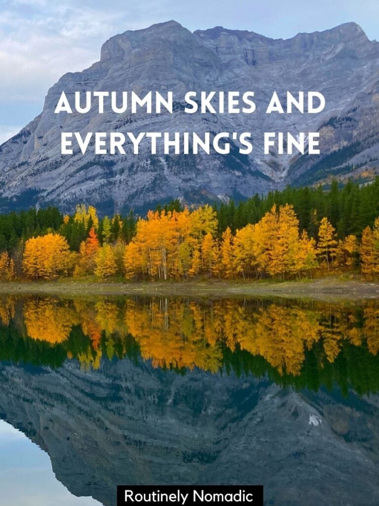 Mountain and yellow trees reflected in a lake with autumn captions for Instagram that reads autumn skies and everything's fine